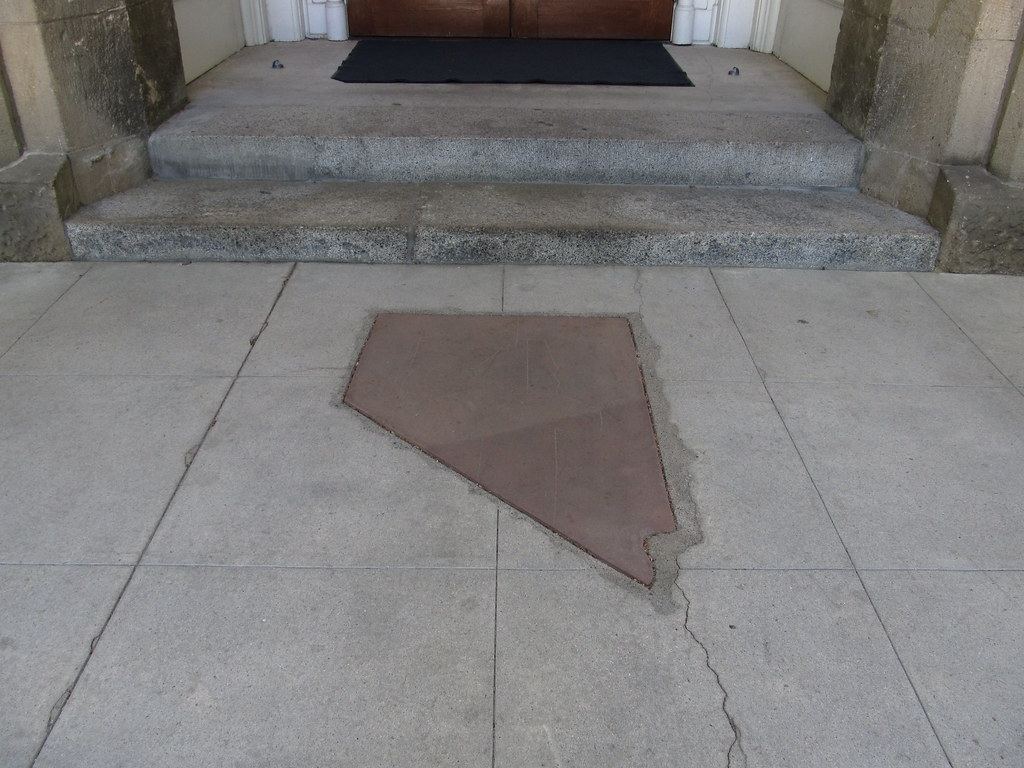 A Nevada-shaped stone inlay in the pavement in front of granite steps leading to a wooden door