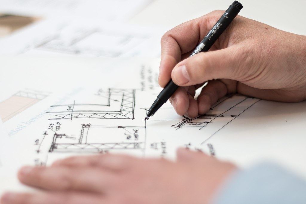 Close-up of a hand sketching architectural construction details on paper with a black pen
