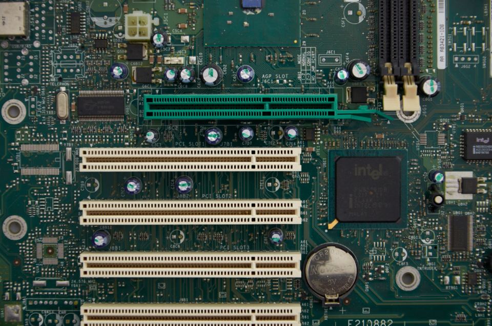 Close-up of a green computer motherboard with expansion slots, chips, capacitors and a coin battery