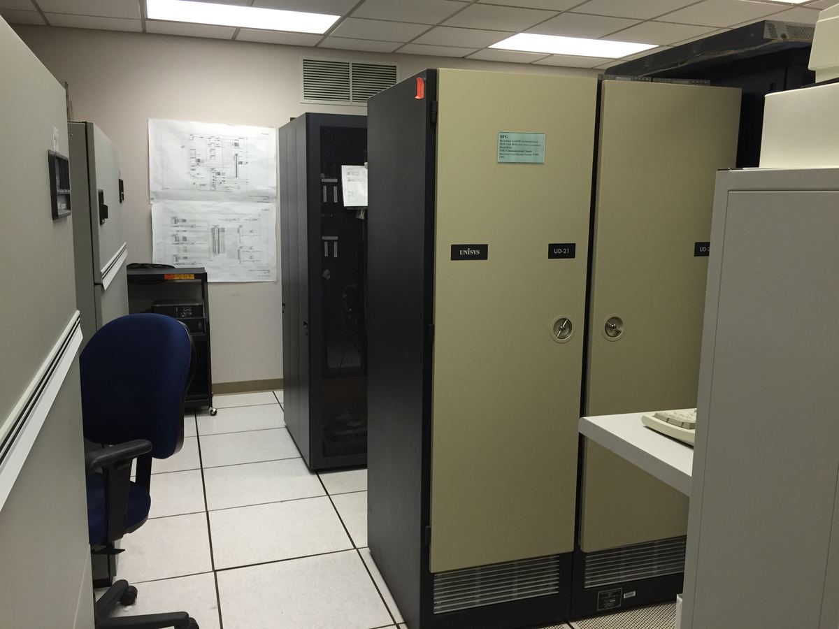 Server cabinets and computer equipment in a small room with a raised tile floor and a blue office chair