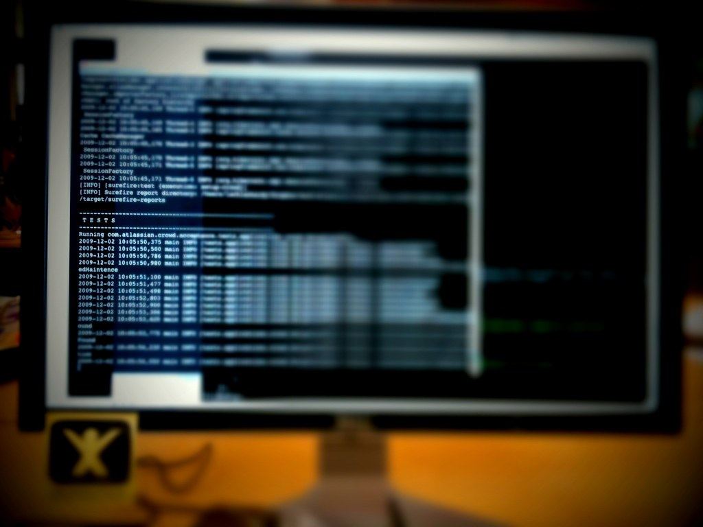 A blurred computer monitor on a desk displays lines of white terminal text against a dark background