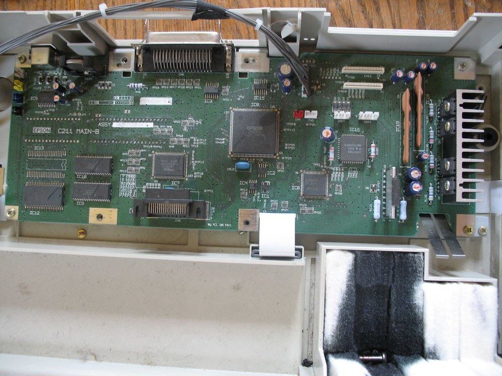 Close-up of a green printer circuit board with chips, capacitors and connectors inside an opened plastic casing