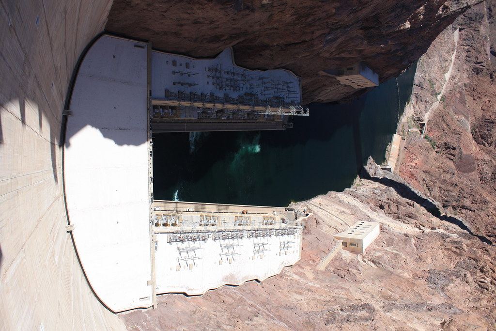 Looking down the curved concrete face of Hoover Dam to its power plant and the green Colorado River in a rocky canyon