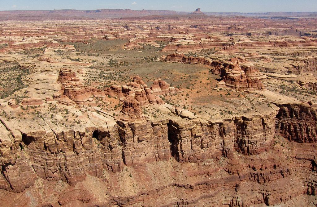 Aerial view of layered red sandstone cliffs, rock spires and scrubby desert plateaus stretching to the horizon