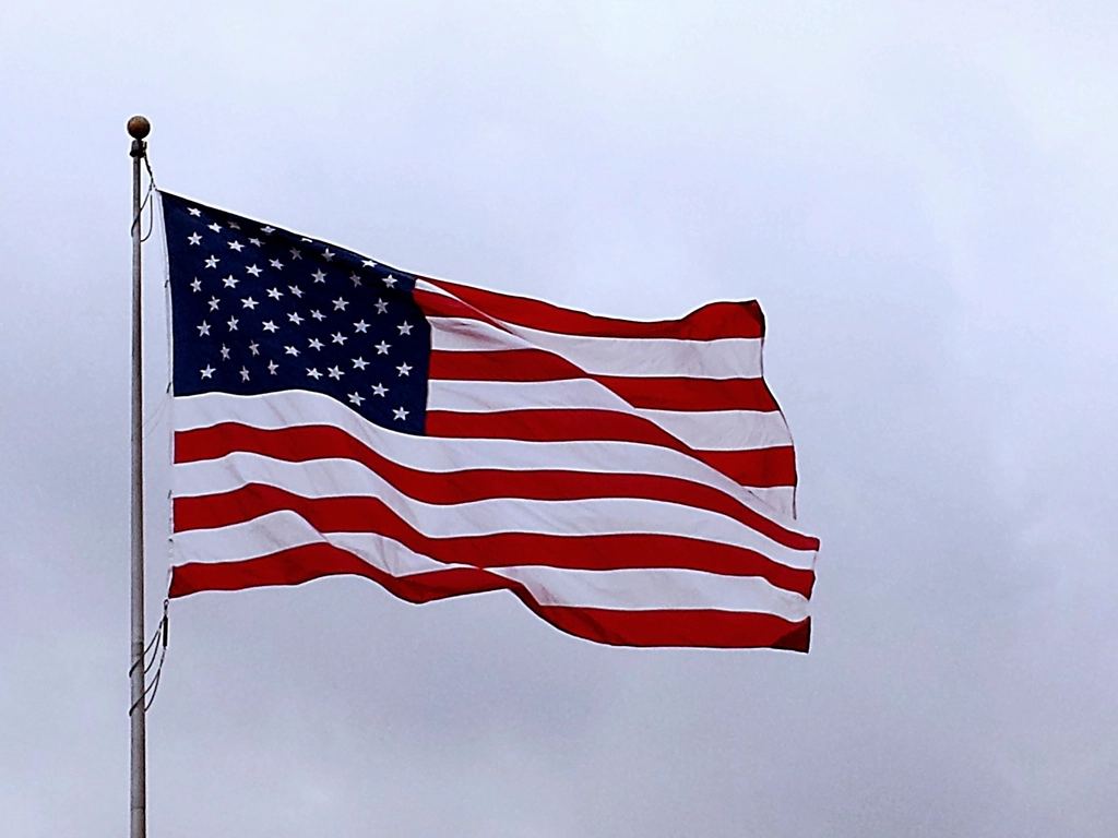 An American flag on a pole waves against a gray, overcast sky
