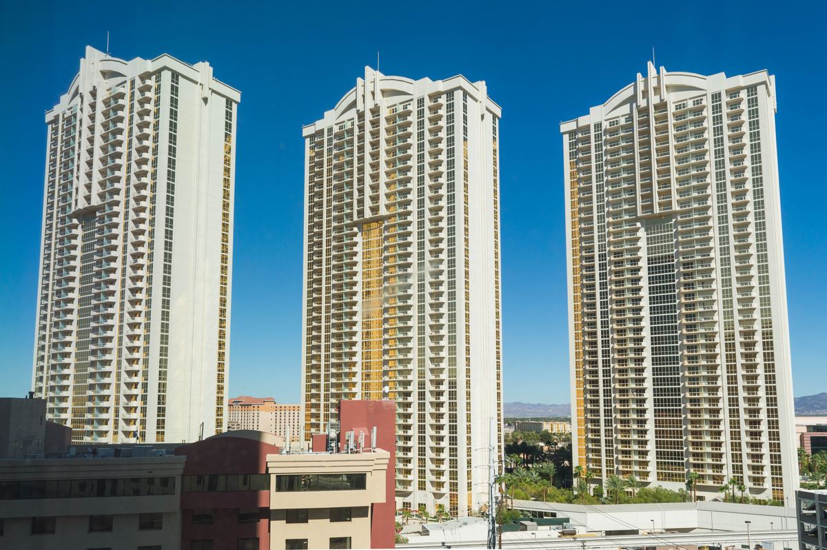 Three tall white high-rise towers with gold-tinted windows under a clear blue sky, with palm trees below