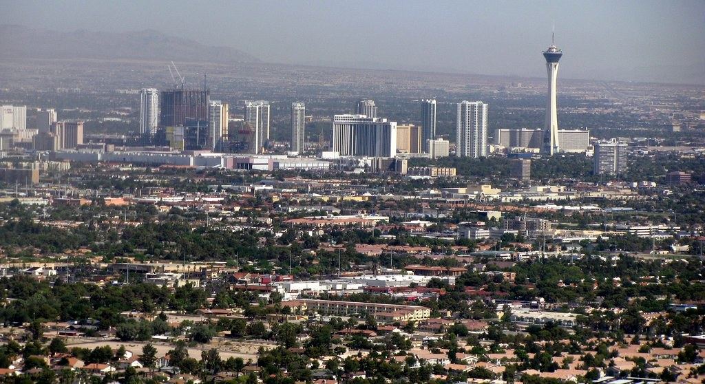 Aerial view of Las Vegas with high-rise towers and a tall observation tower rising beyond tree-lined neighborhoods