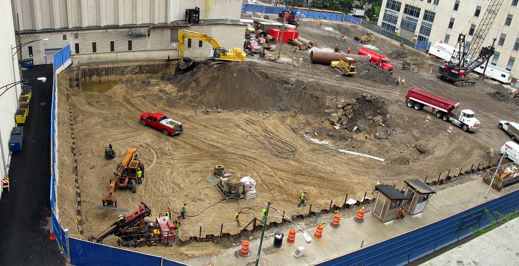 Aerial view of a large excavated construction site with excavators, trucks and workers in hard hats