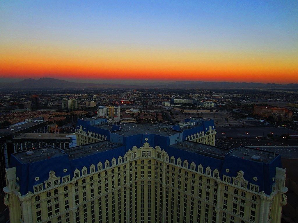 Ornate hotel tower with blue roofs overlooking a sprawling city and distant mountains under an orange sunset sky
