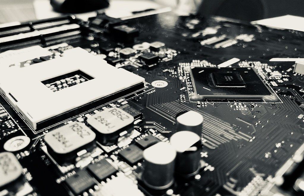 Black-and-white close-up of a computer motherboard with an empty CPU socket, chips and capacitors