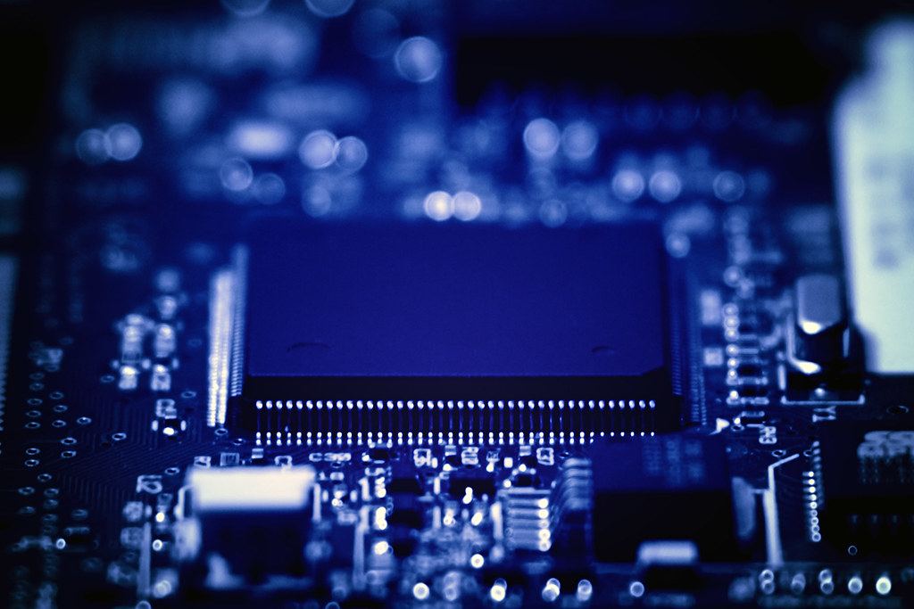 Close-up of a microchip on a circuit board with surrounding components, lit in blue tones