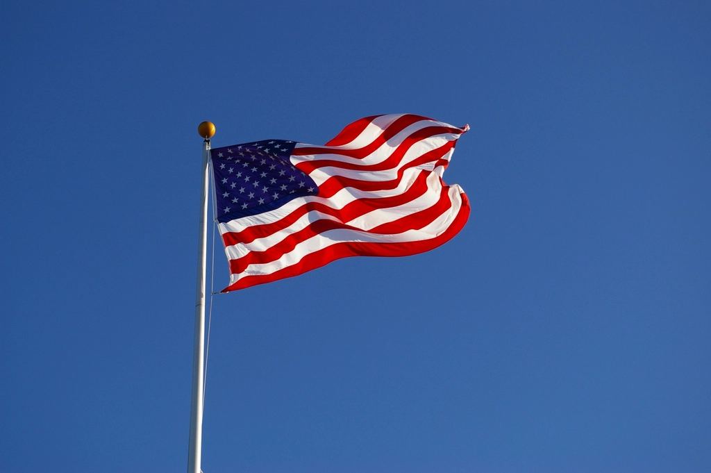 An American flag waves on a white flagpole against a clear blue sky