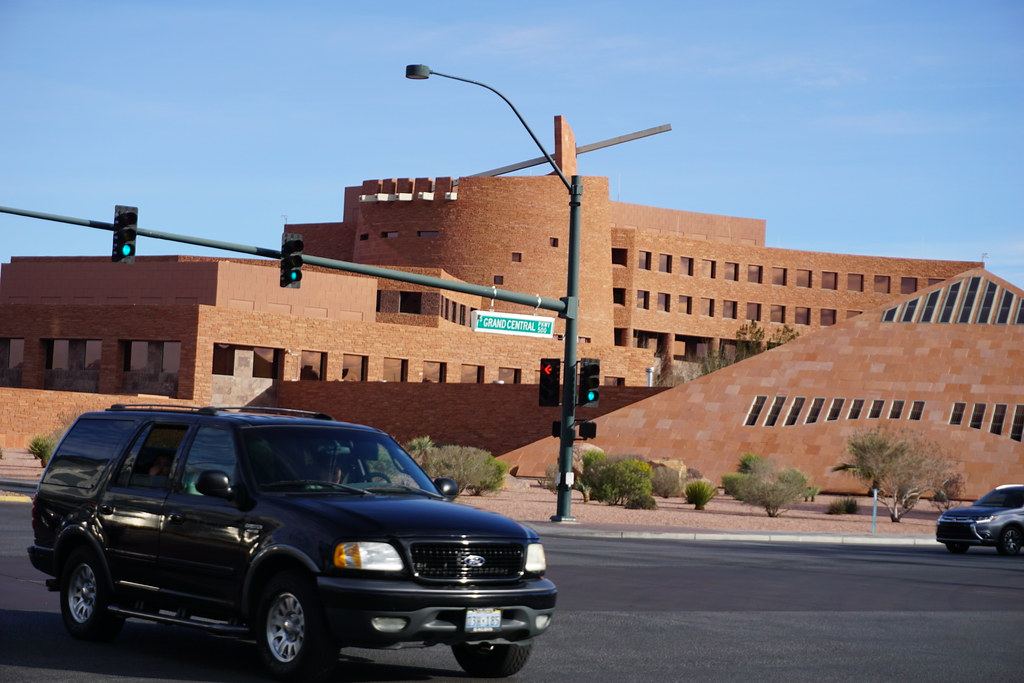 Red sandstone government building with a pyramid-shaped wing behind a traffic light and a black SUV on the street