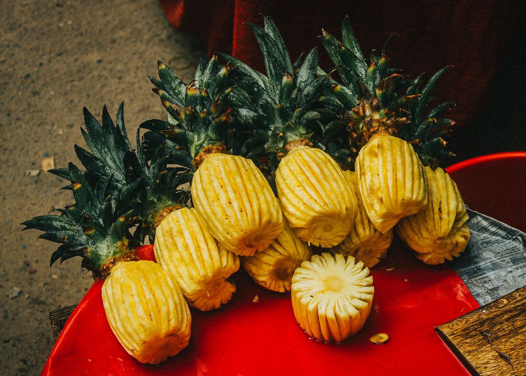 Peeled fresh pineapples with leafy tops piled on a red tray at an outdoor street food stand
