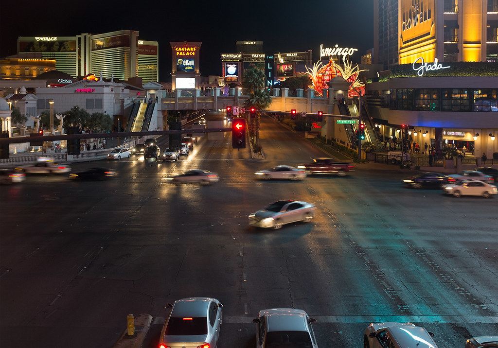 Night view of a busy Las Vegas Strip intersection with blurred cars and lit casino signs