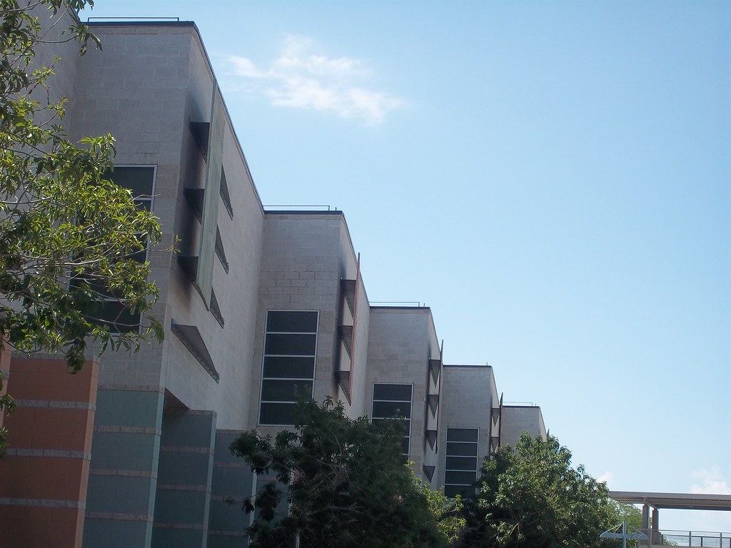 Exterior of a multi-story concrete block campus building with tall windows, trees and blue sky