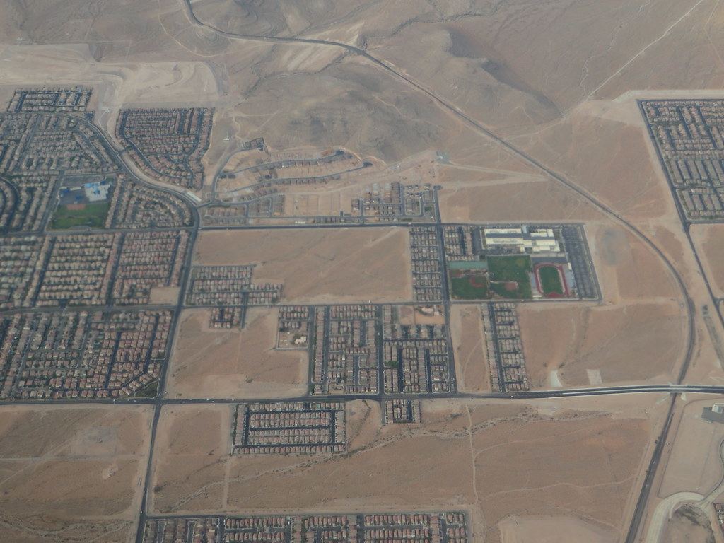 Aerial view of desert suburbs with housing tracts and a school campus with athletic fields and a running track