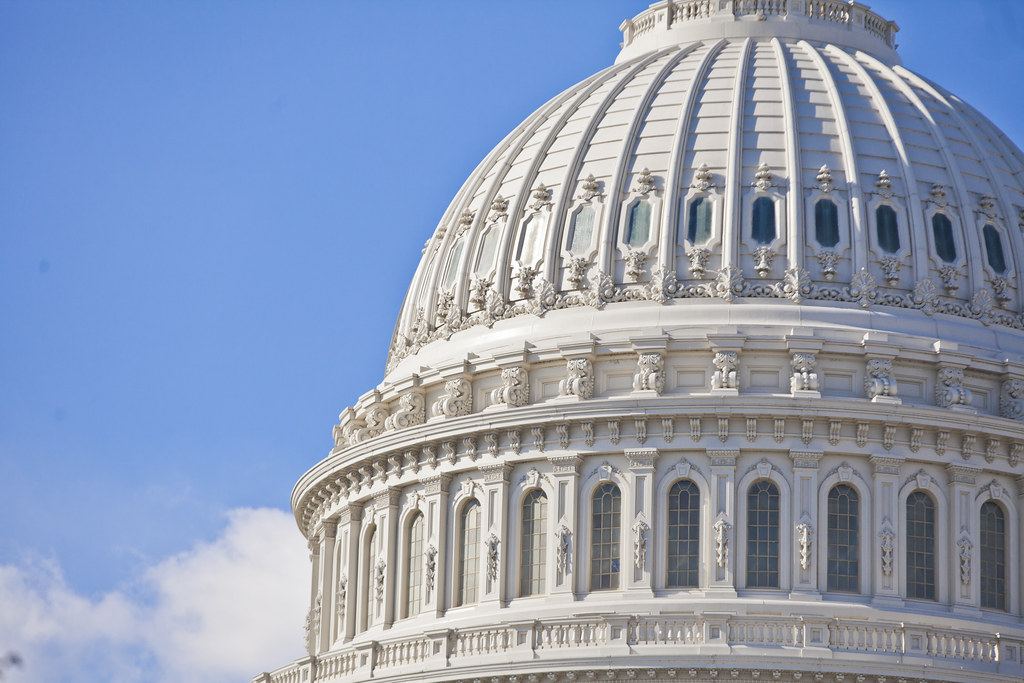 Close-up of the white U.S. Capitol dome with ornate columns and windows against a blue sky