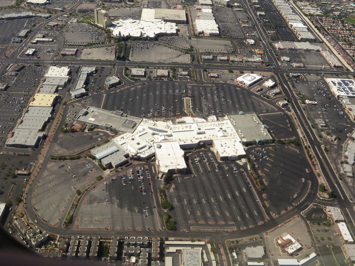 Aerial view of a large shopping mall surrounded by parking lots and roads in a desert suburb
