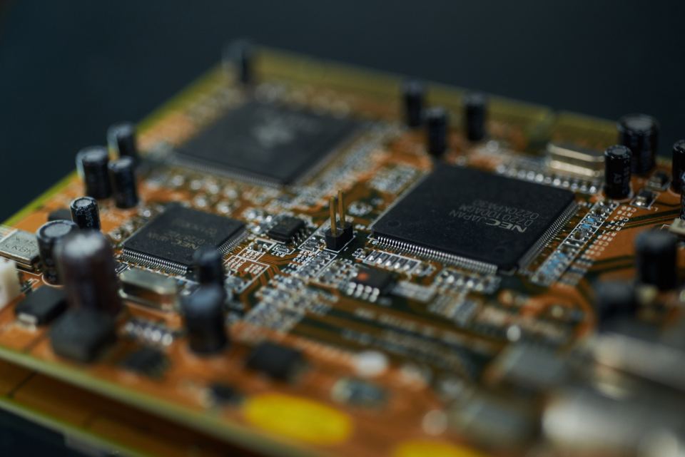 Close-up of an orange circuit board with black microchips and capacitors, shot with shallow focus