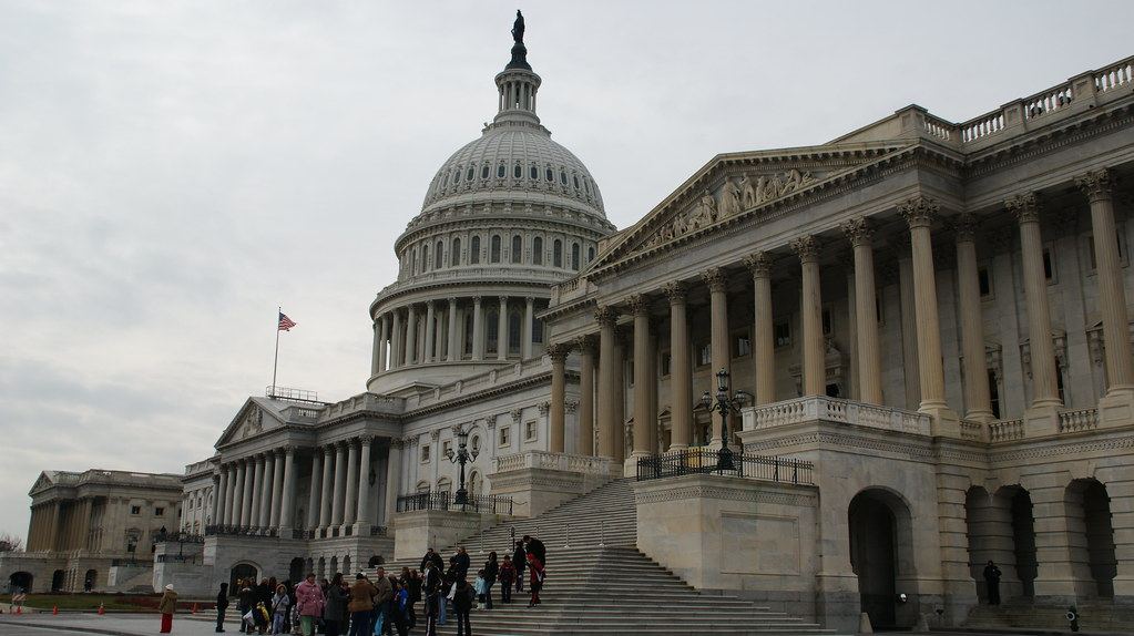The domed U.S. Capitol building under an overcast sky, with a group of people gathered near its front steps