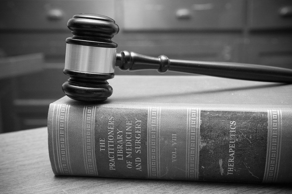 Black-and-white photo of a wooden gavel resting on an old hardbound medical reference book on a table