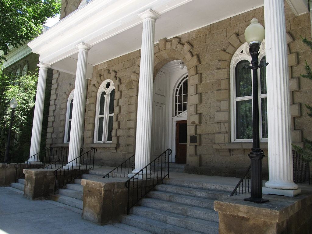 Sandstone building entrance with white fluted columns, arched windows, stone steps and black lampposts
