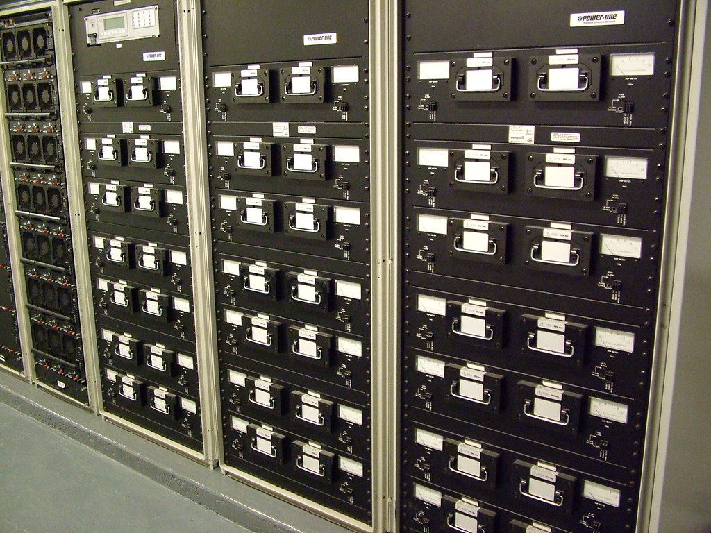 Rows of black equipment racks with handled modules, gauges and switches lined up along a gray floor