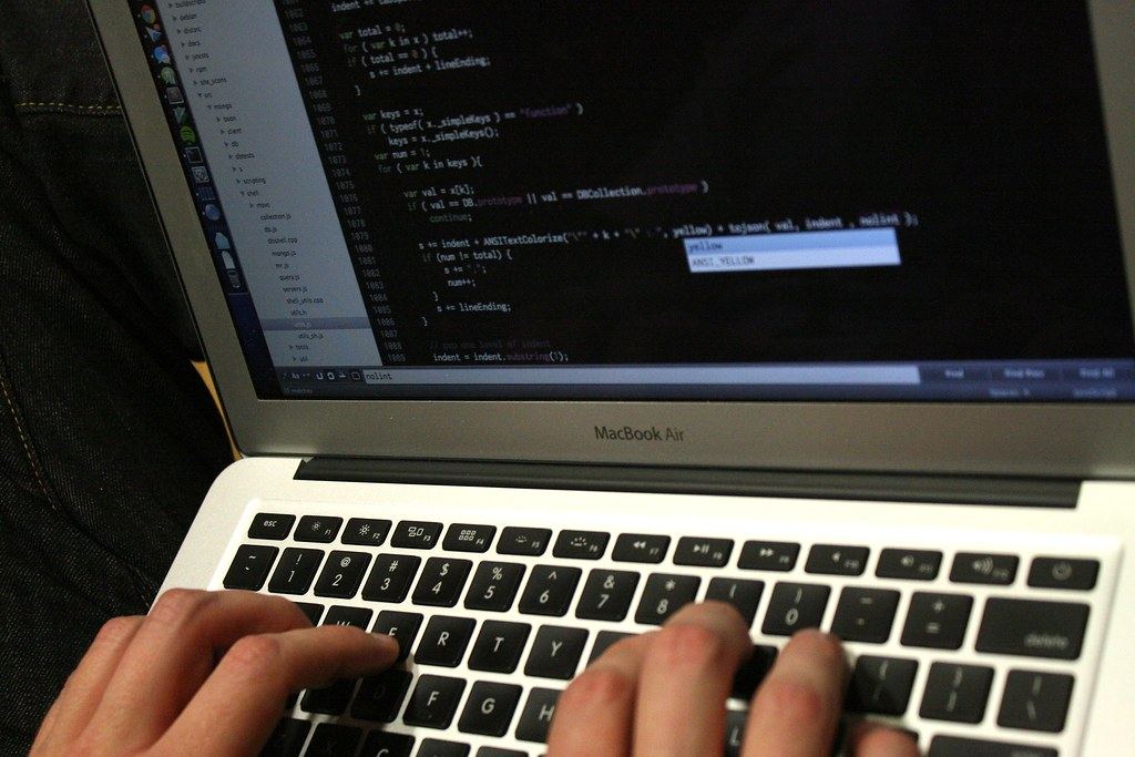 Hands typing on a laptop keyboard while the screen shows lines of programming code in a text editor