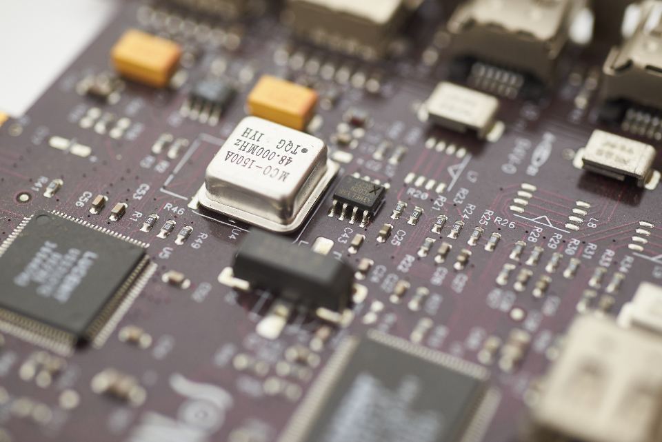 Close-up of a dark circuit board with a silver crystal oscillator, microchips and small electronic components