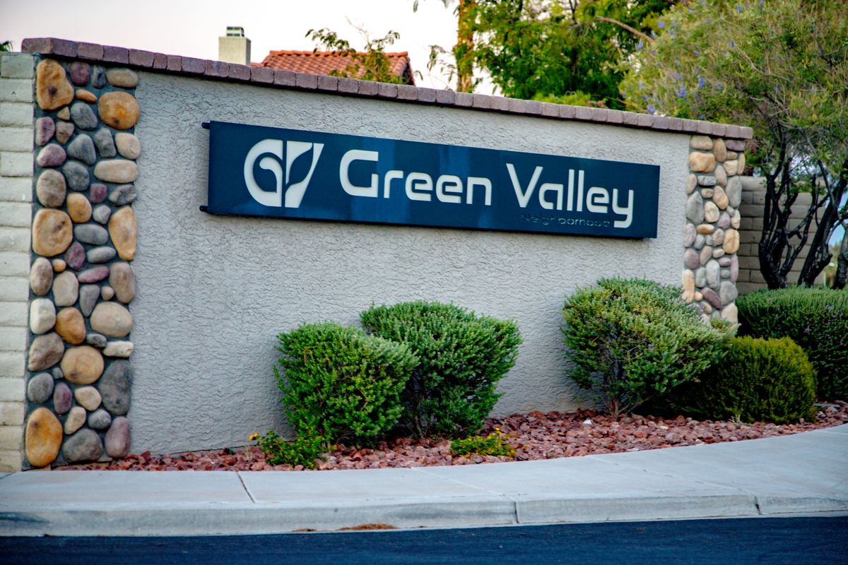 Green Valley Neighborhood sign on a stucco and river-rock wall with trimmed shrubs beside a curb
