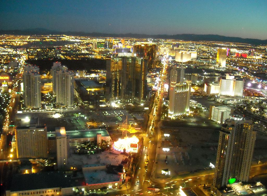 Aerial view of the brightly lit Las Vegas Strip and surrounding high-rise hotels at dusk, with mountains behind
