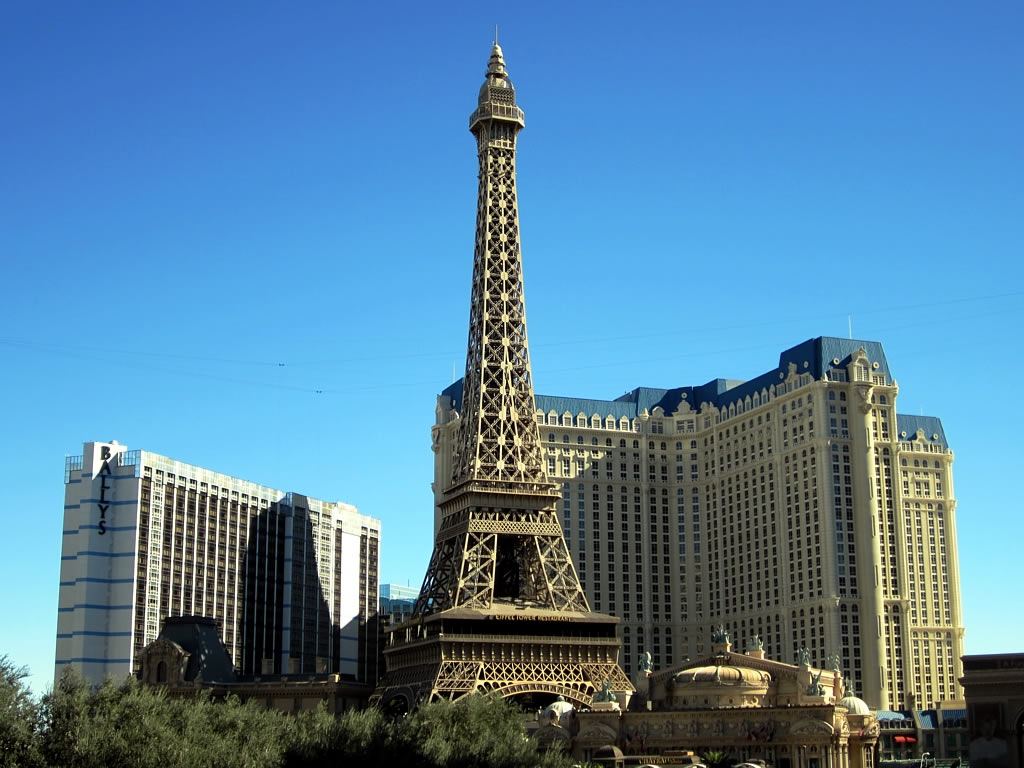 Replica Eiffel Tower in front of a large hotel tower and a high-rise building under a clear blue sky