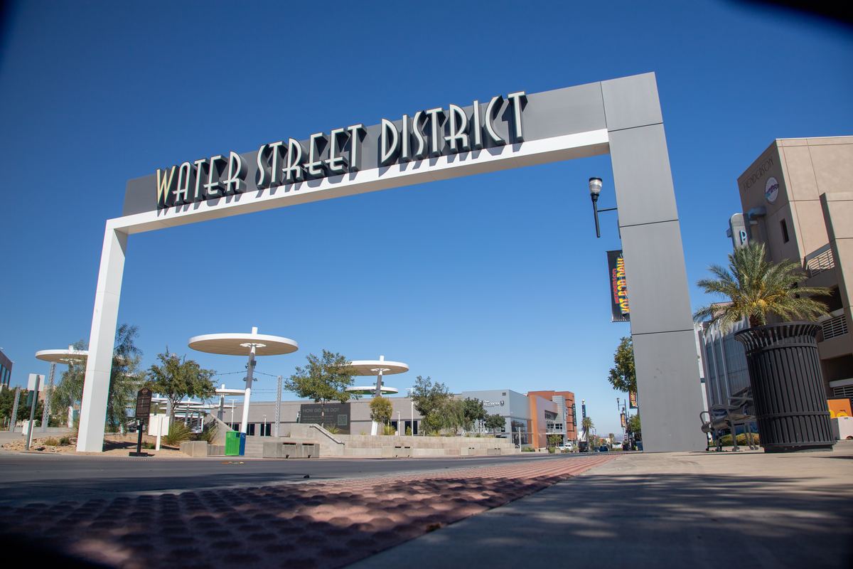 A large Water Street District archway sign over a downtown street with palm trees and buildings under a blue sky