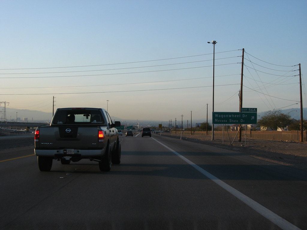 A pickup truck drives on a desert highway past a green exit sign for Wagonwheel Dr and Nevada State Dr at dusk