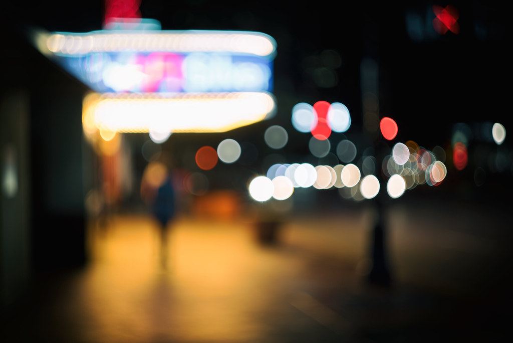 Blurred night view of a glowing theater marquee and city lights along a sidewalk