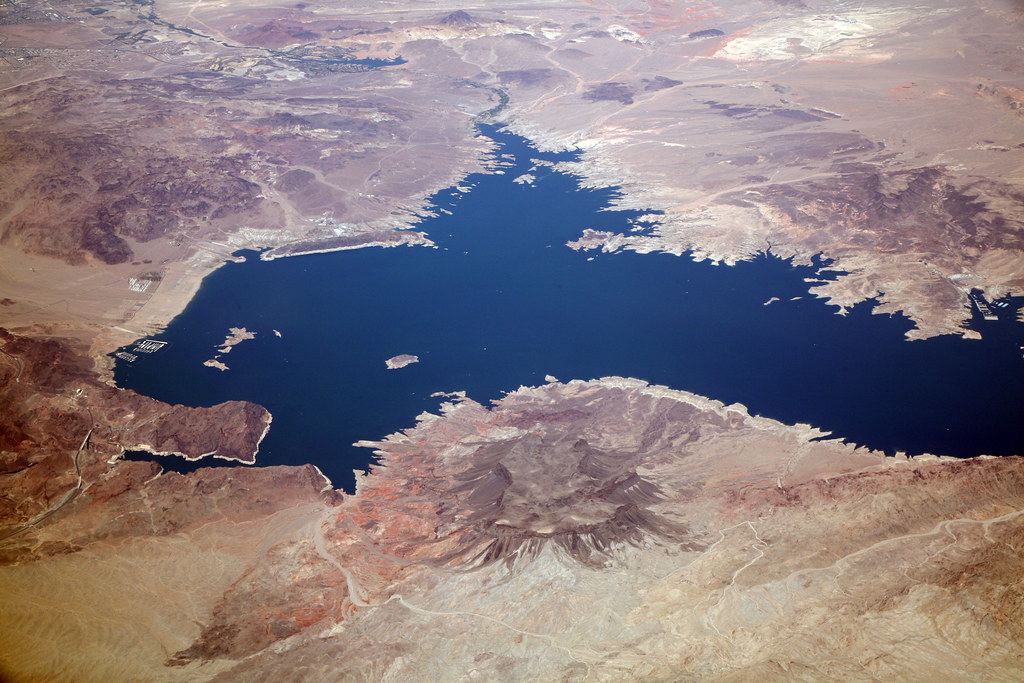 Aerial view of a deep blue desert lake surrounded by rugged brown mountains and pale shoreline bathtub rings