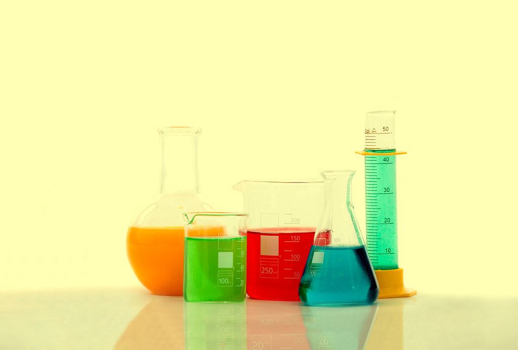 Laboratory beakers, a flask and a graduated cylinder filled with orange, green, red and blue liquids