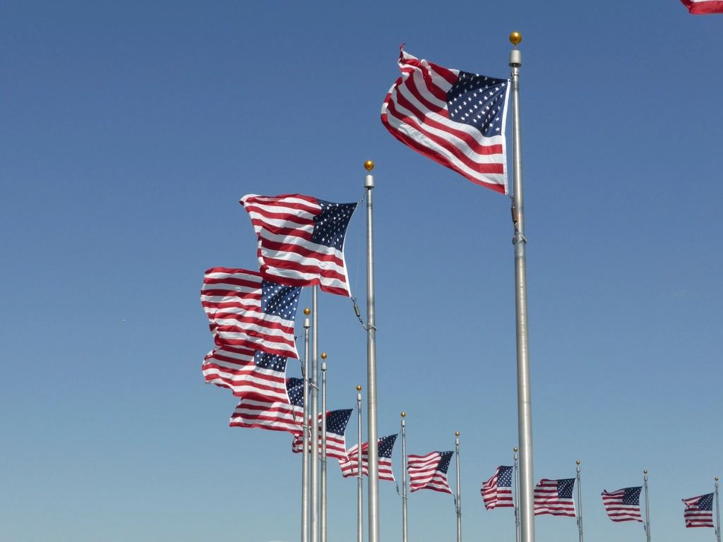 A row of American flags on tall poles flapping in the wind against a clear blue sky