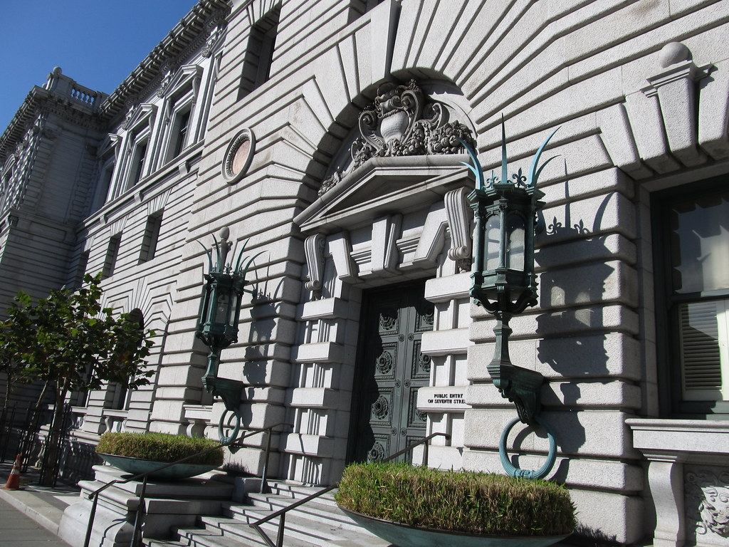 Ornate granite courthouse entrance with carved arch, bronze doors, green lanterns and planters on the steps