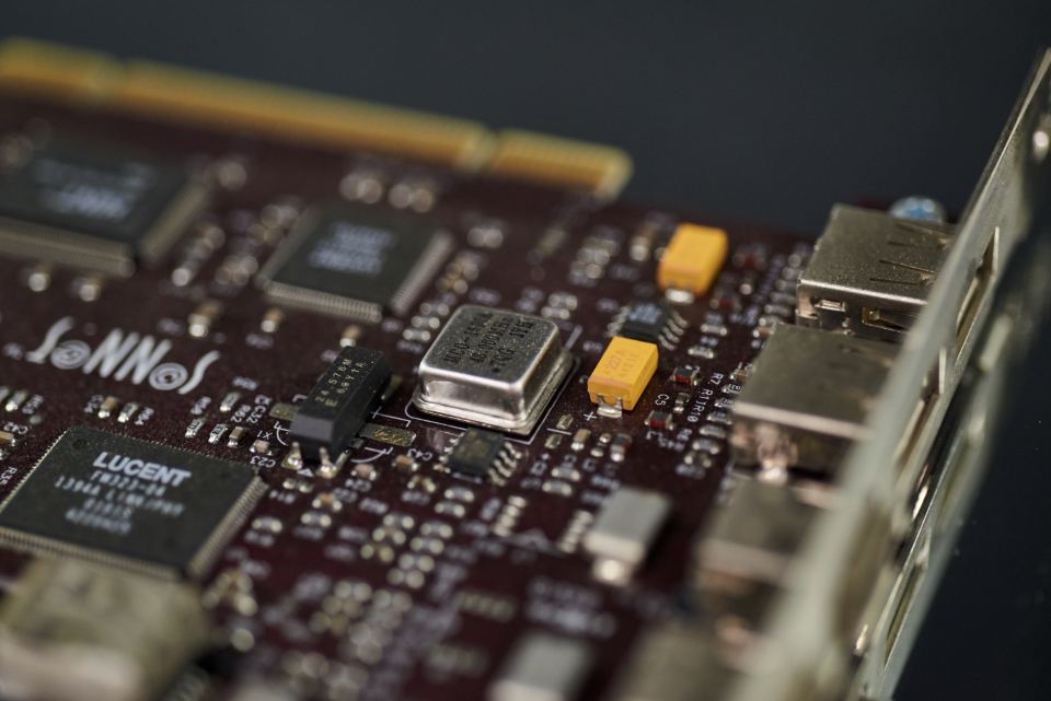 Close-up of a dark red computer circuit board with chips, a metal oscillator, yellow capacitors and USB ports