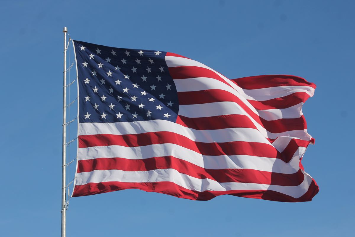 An American flag waves from a metal flagpole against a clear blue sky