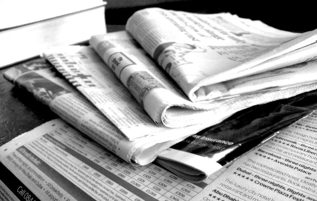 Black-and-white photo of several folded newspapers stacked on a table