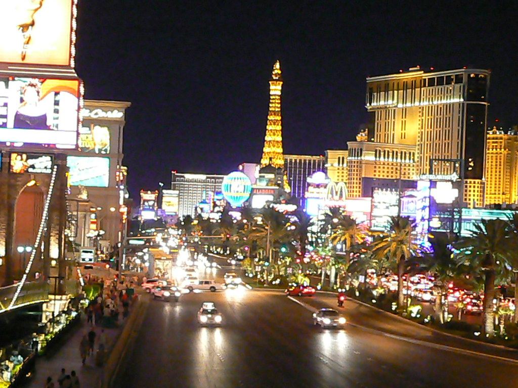 Las Vegas Strip at night with traffic, palm trees, casino lights and an Eiffel Tower replica in the distance