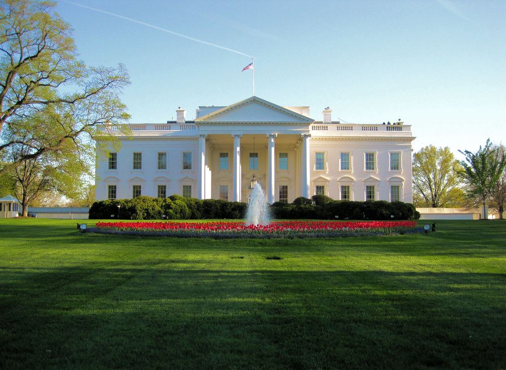 The White House north facade with a fountain and red tulip bed on a green lawn under a clear blue sky