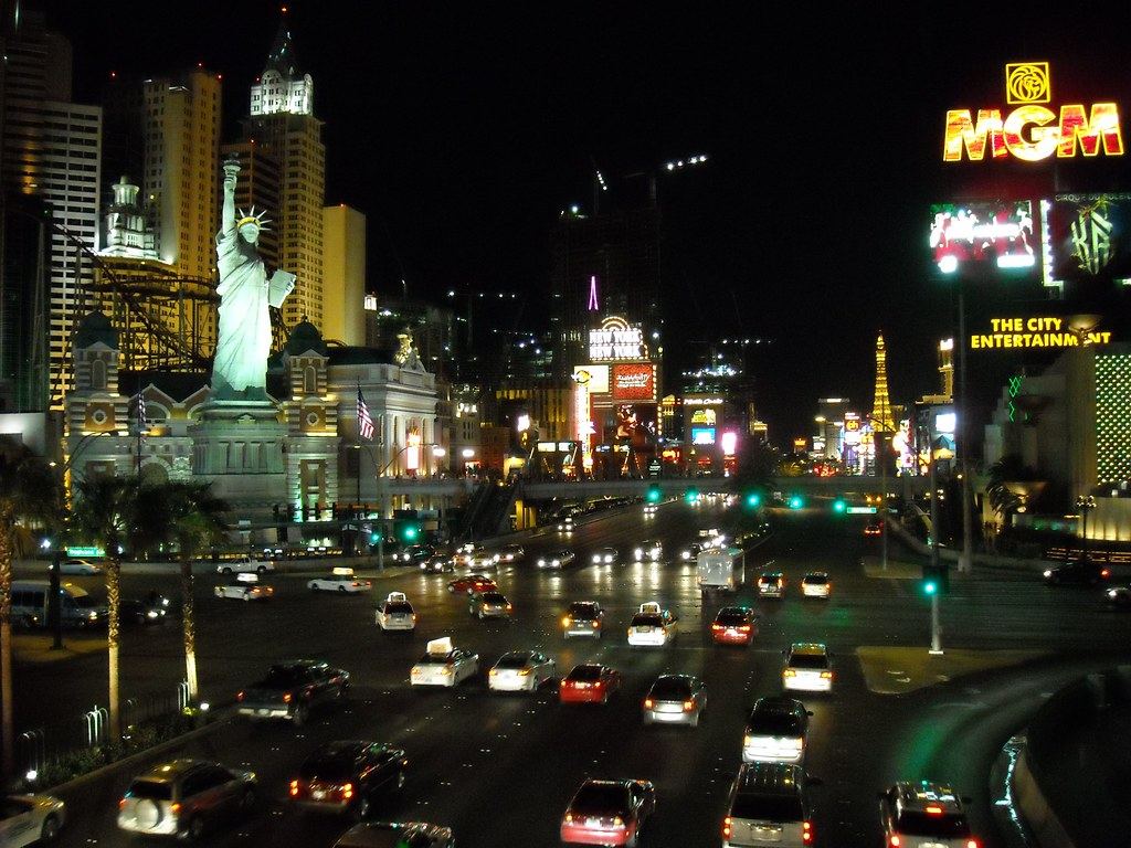 Traffic fills the Las Vegas Strip at night beside a Statue of Liberty replica and brightly lit casino signs