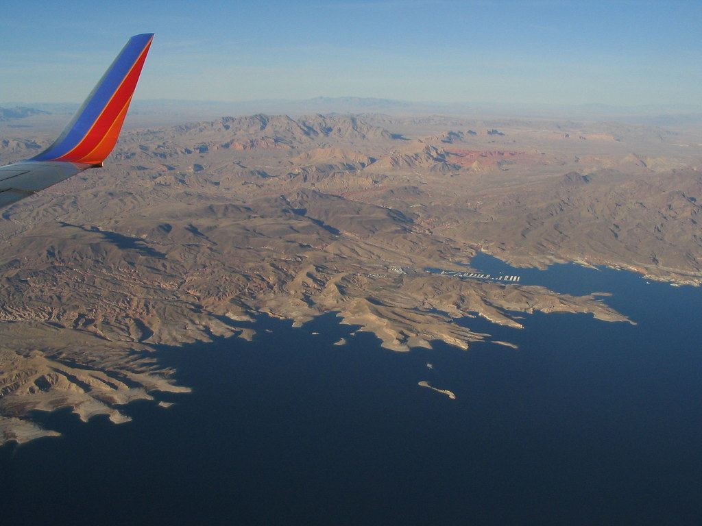 Aerial view from a plane window of a deep blue lake bordered by rugged brown desert mountains and a marina