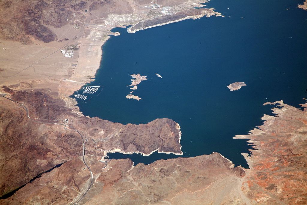 Aerial view of a deep blue desert lake with rocky shoreline, small islands, marinas and a winding road
