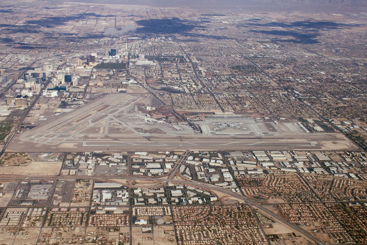 Aerial view of a large airport with runways, surrounded by sprawling desert city neighborhoods and high-rise towers