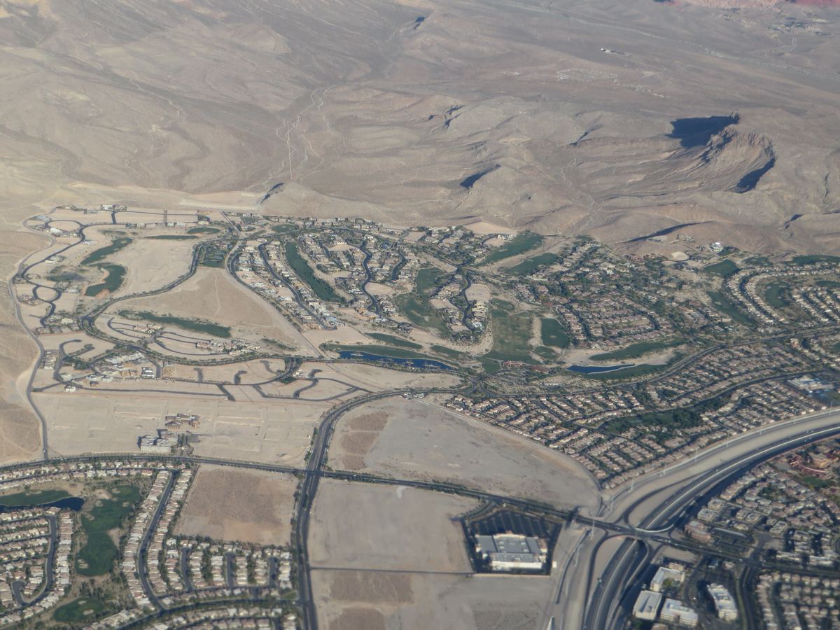 Aerial view of suburban housing developments, golf courses and highways at the edge of desert mountains